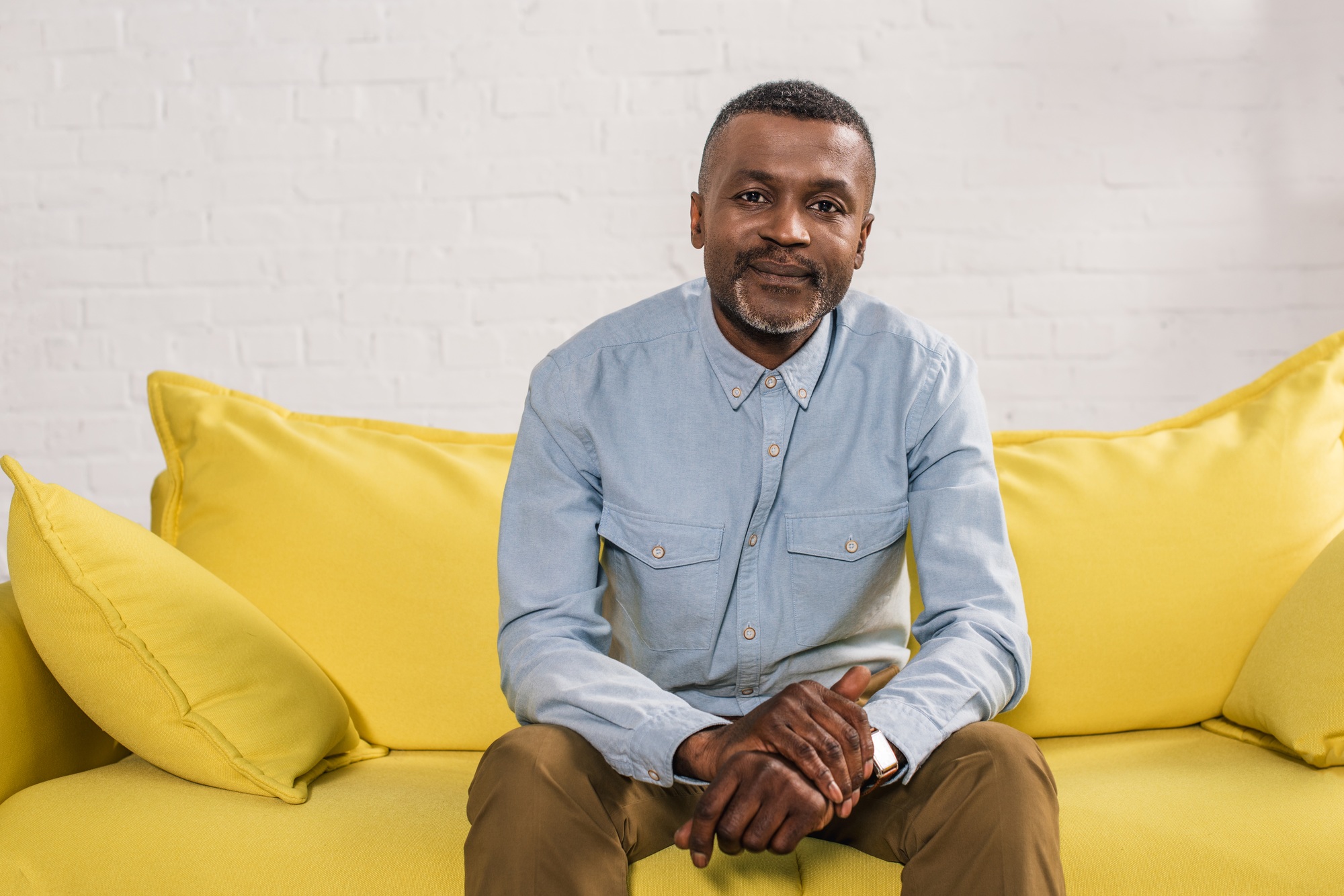 senior african american man sitting on yellow couch and smiling at camera